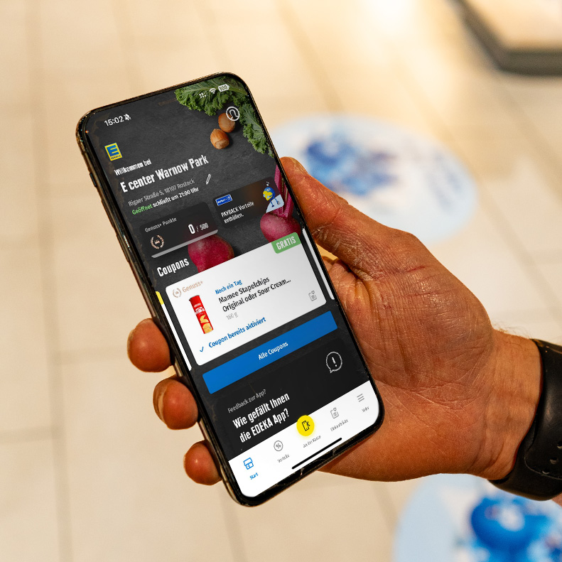 Mitarbeitende Person des E center Warnow Parks zeigt EDEKA App.