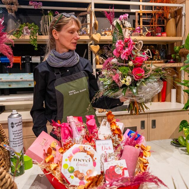 Mitarbeiterin aus dem E center Warnow Park präsentiert Blumenstrauß und Geschenkkorb