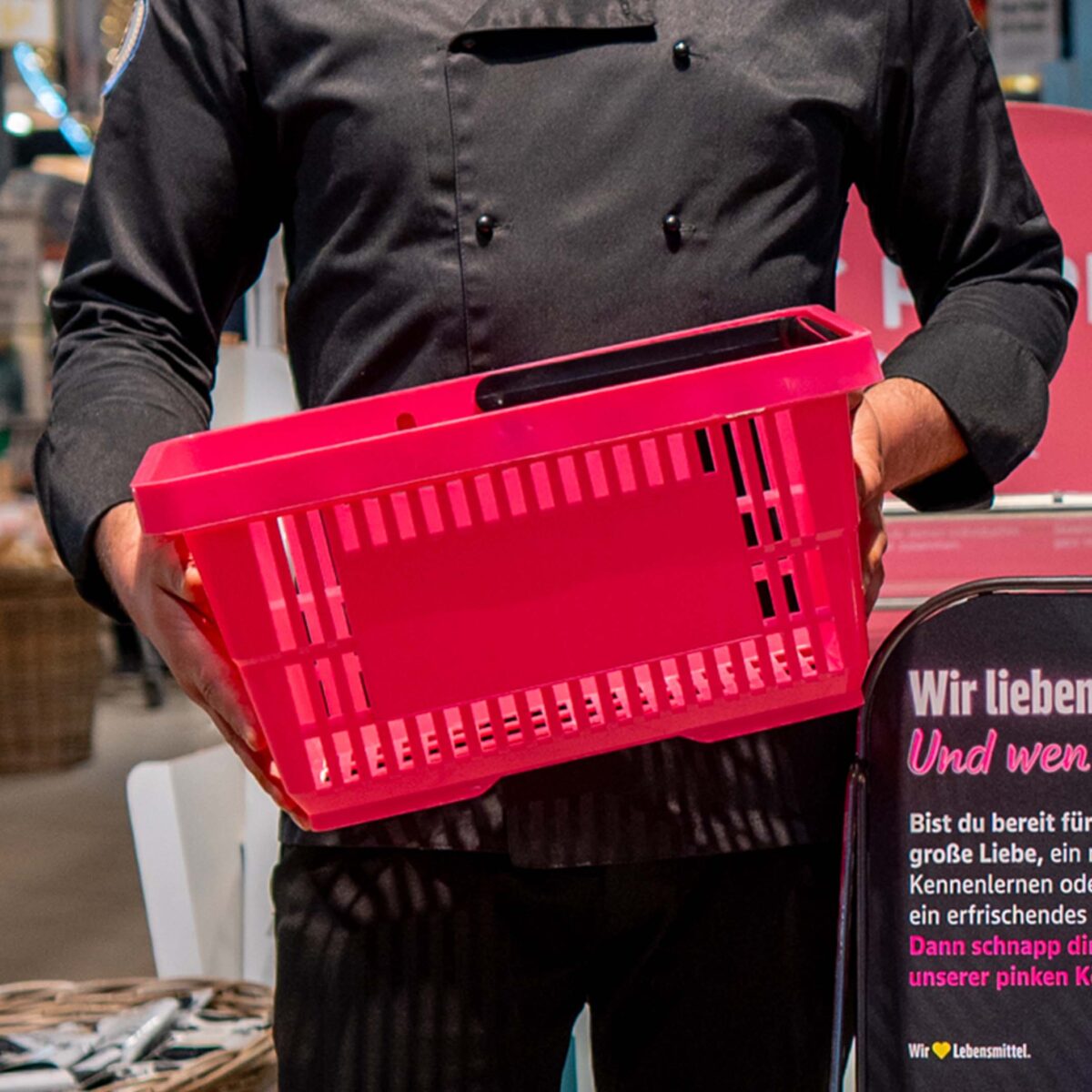 Mitarbeiter präsentiert rosa Einkaufskörbe aus dem E center Warnow Park.