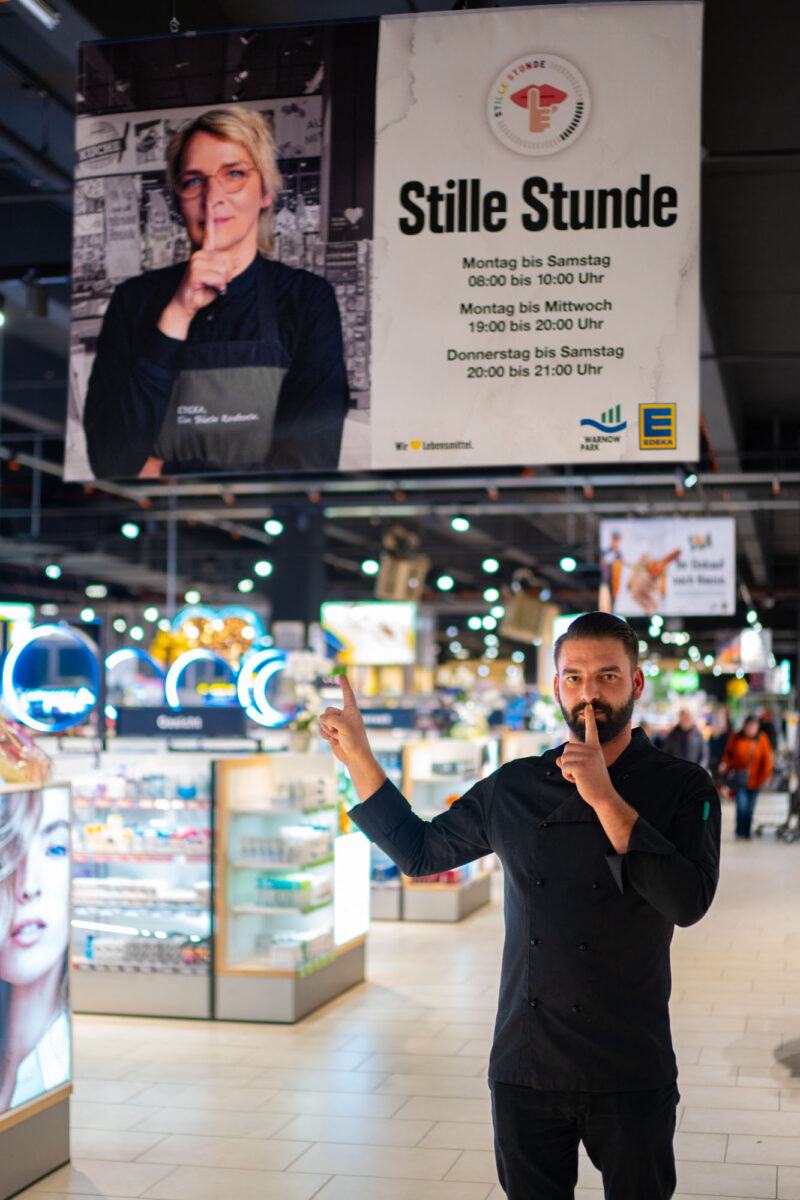 Mitarbeiter aus dem E center Warnow Park hält sich den Finger vor den Mund, symbolisch für die Stille Stunde